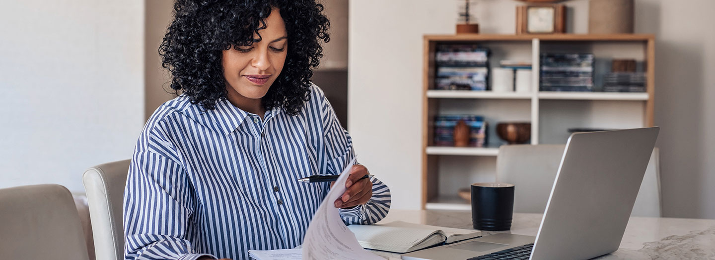 Smiling woman organizing paperwork in front of her computer.