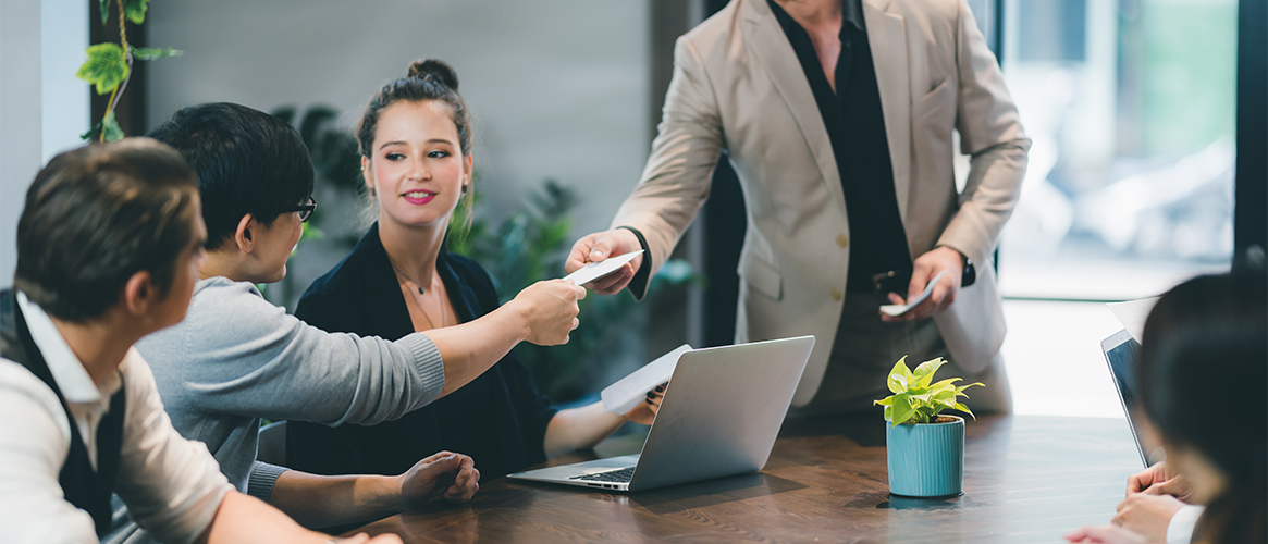 Insurance employee hands certificate to client at a conference table meeting.