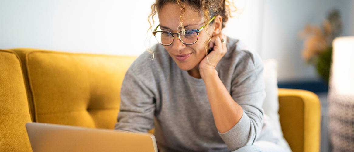 Woman sitting on a yellow couch working on a laptop computer.