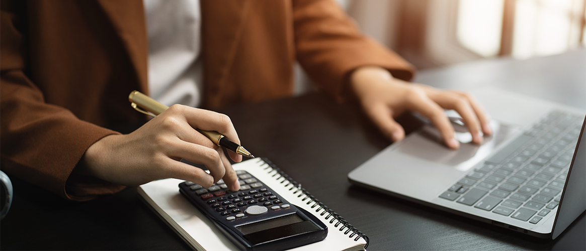 Woman using calculator and typing in figures on a computer.