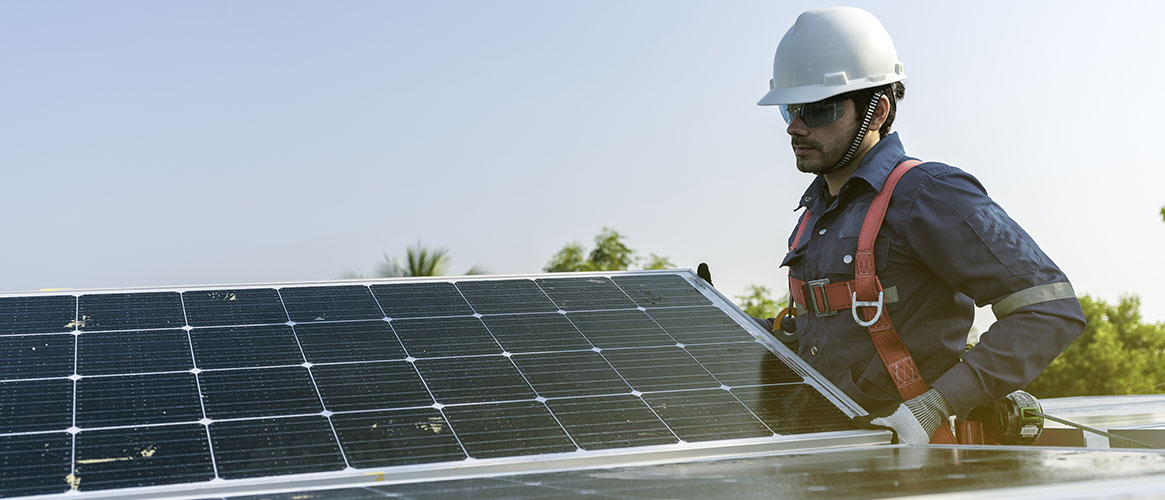 Solar panel installer working on a roof wearing fall protection.