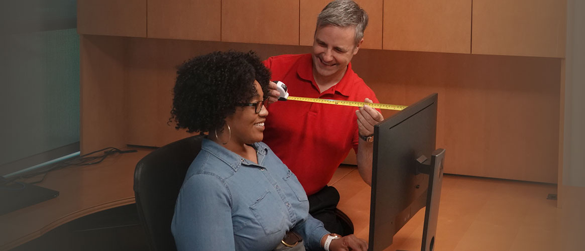 Employee receiving ergonomic evaluation of workspace monitor, chair and desk